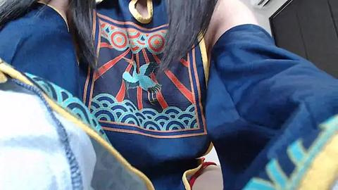 Media: A video of a woman in a blue and gold traditional Chinese dress with intricate patterns and a phoenix design. The focus is on her chest, with her long black hair partially visible.