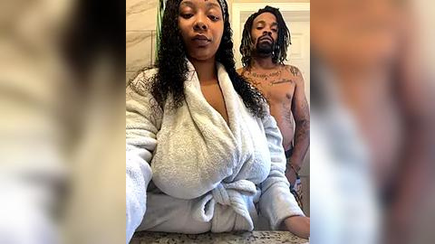 Media: Video of a Black woman with curly hair in a white bathrobe and a Black man with dreadlocks, both nude, in a bathroom.