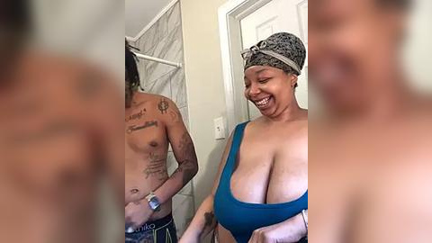 Media: Video of a happy, topless Black woman with large breasts in a teal tank top, standing beside a shirtless Black man with tattoos, in a bathroom with a mirror and white door.