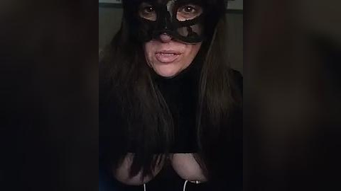 Media: Video of a woman in a black mask, dark hair, and black top, with dramatic lighting creating a mysterious, dark atmosphere.