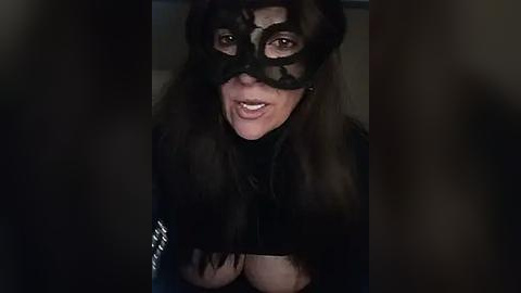 Media: A video of a woman in a dark, black mask with intricate lace patterns, her long dark hair partially visible, and a black top, set against a dimly lit background, creating a mysterious and slightly eerie atmosphere.