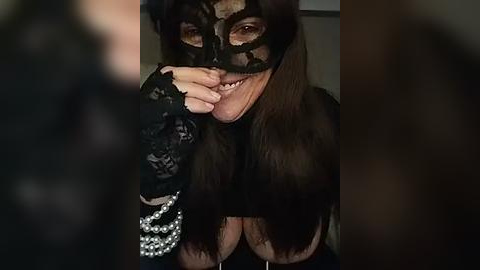 Media: Video of a woman with long brown hair, wearing a black lace mask, revealing a smile, adorned with a pearl necklace.