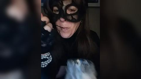 Media: Video of a person with a black mask, long dark hair, and a sinister expression, holding a bag, in a dimly lit room.