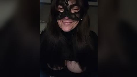 Media: Video of a middle-aged woman with dark hair and fair skin, wearing a black lace mask, smiling widely, eyes partially hidden.