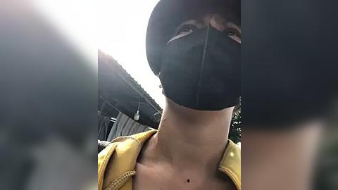 Media: Video of a masked man in a yellow jacket, with a blurred background showing industrial structures. He has a visible tattoo on his neck.