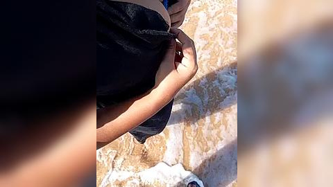 Media: Video of a person in a dark shirt adjusting a light-colored scarf, with a blurred background featuring a rocky terrain and a white object, possibly a bag, on the ground.