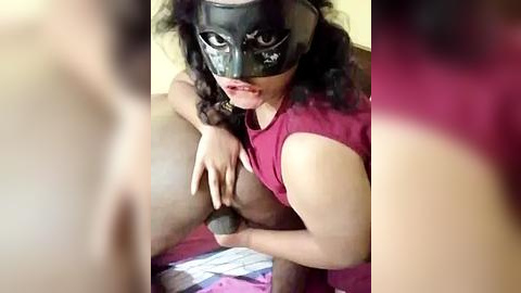 Media: Video of a dark-skinned woman with curly hair and a black mask, licking a penis, wearing a sleeveless maroon top.