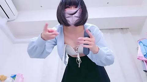 Media: Video of a young East Asian woman with short black hair, wearing a light blue unbuttoned jacket, revealing a white lace bra, and a black skirt, gesturing playfully in a white room with a white curtain and air conditioner.