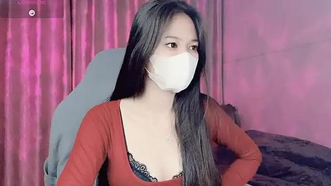 Media: Video of an Asian woman with long black hair, wearing a white mask, red top, and black lace bra, sitting indoors with pink curtains and gray chair.