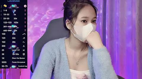 Media: Video of a young Asian woman in a blue cardigan and white mask, seated in a chair against a purple-lit backdrop. On-screen, a live stream displays her heart rate, temperature, and other metrics.