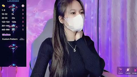 Media: Video of an East Asian woman with long black hair, wearing a black ribbed sweater and a white face mask, sitting against a purple and pink gradient background.