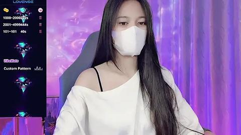 Media: Video of an Asian woman with long black hair, wearing a white off-shoulder top, face mask, and a custom filter with blue and green lights in the background.