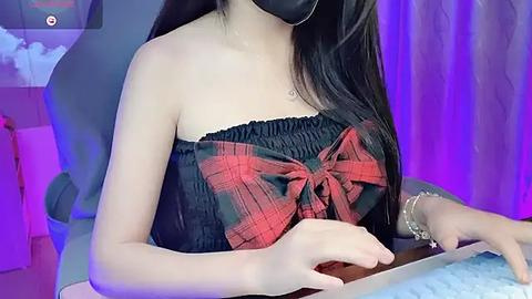 Media: Video of an Asian woman with long black hair, wearing a black strapless top with a red plaid bow, black face mask, and silver bracelets, playing a keyboard.