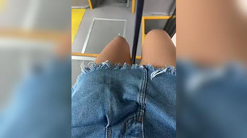 Media: Video of a person wearing light blue denim shorts with frayed hems, seated on a public bus. The bus seat is gray with yellow accents, and the person's legs are crossed, highlighting the denim's texture and the bus's interior.