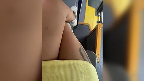 Media: Video of a light-skinned woman in a yellow skirt, sitting on a bus seat with her legs crossed, showing a tattoo on her thigh.