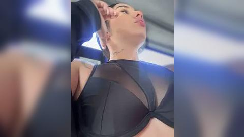 Media: A video of a woman in a black sheer bra, with a tattoo on her neck, captured from a low angle, showcasing her cleavage and toned physique.