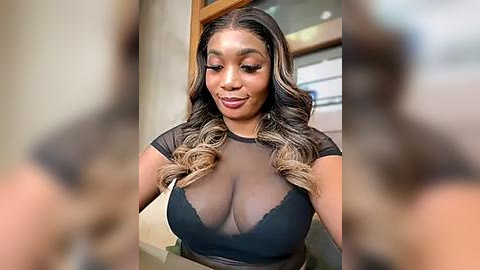 Media: Video of a curvy Black woman with long, wavy, dark-brown hair, wearing a sheer black top revealing her ample cleavage. She's smiling, with makeup accentuating her features. Background is blurred, focusing on her.