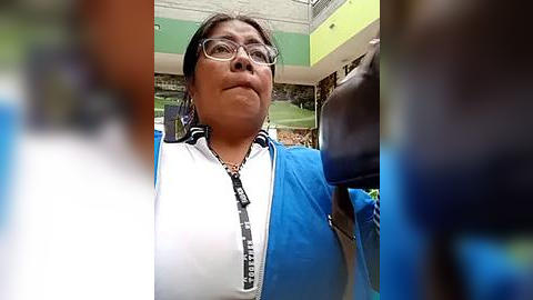 Media: A video of a middle-aged Asian woman with glasses, wearing a blue and white cycling jersey, holding a microphone in a gymnasium.