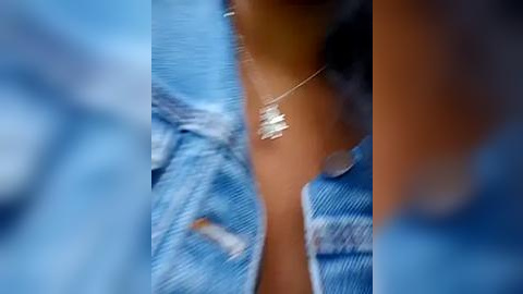 Media: A close-up video of a person wearing a blue denim jacket with a white graphic design on the left sleeve. A delicate silver necklace with a small, intricate pendant hangs around their neck. The background is blurred, focusing on the jacket and necklace details.