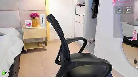 Media: Video of a modern, minimalist bedroom with a black office chair facing a mirror, white dresser, and a small nightstand with pink flowers and a vase.