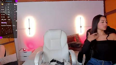 Media: Video of a modern, dimly-lit living room with white leather armchair, woman in black top and jeans, and wall-mounted lamps.