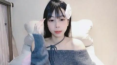 Media: A video of an Asian woman with long black hair and a white headband, wearing a blue towel, sitting in a white chair.