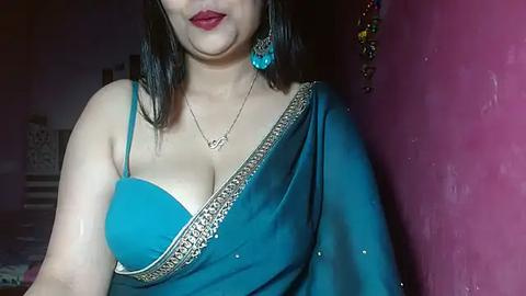 Media: Video of a woman with medium skin tone, wearing a turquoise sari with gold embroidery, blue earrings, and a silver necklace.