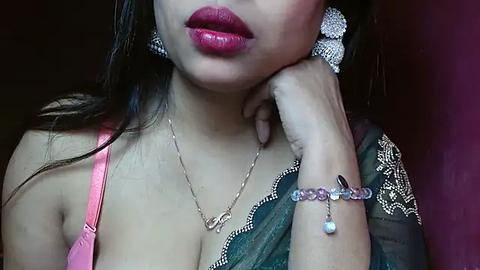 Media: Video of a South Asian woman with medium skin tone, wearing a pink bra, dark green sari, and silver jewelry.