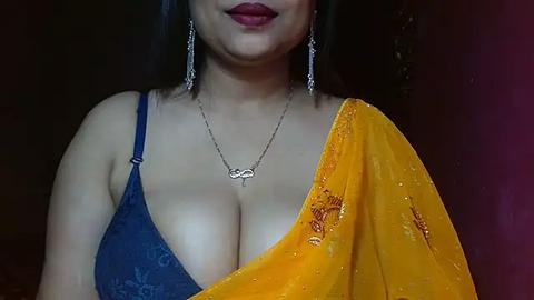 Media: A video of a South Asian woman with medium skin tone, wearing a blue lace bra and a yellow saree with intricate embroidery. She has long black hair and red lipstick.