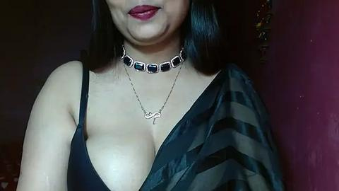 Media: Video of a woman with medium skin tone, black hair, wearing a black bra, a black and white striped fabric, and a silver necklace with a heart pendant.