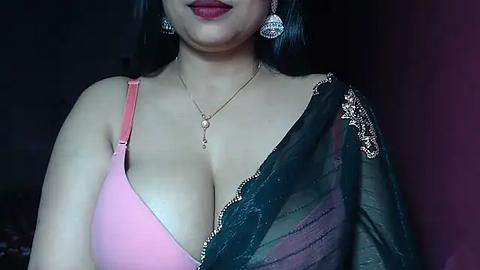 Media: Video of a light-skinned woman with long black hair, wearing a pink bra and black saree, adorned with a diamond necklace and matching earrings.