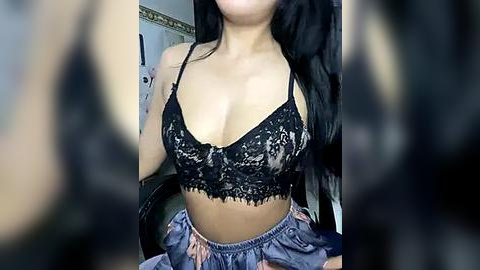 Media: Video of an Asian woman with long black hair, wearing a black lace bralette revealing cleavage and a high-waisted, patterned skirt, sitting indoors with blurred background.