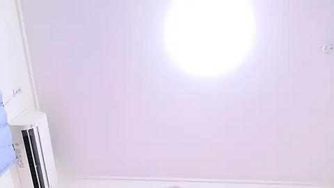 Media: A video of a minimalist, bright white room with a central circular light source emitting a soft glow. On the left, a light blue towel hangs from a white rack. The walls and ceiling are pristine and smooth.