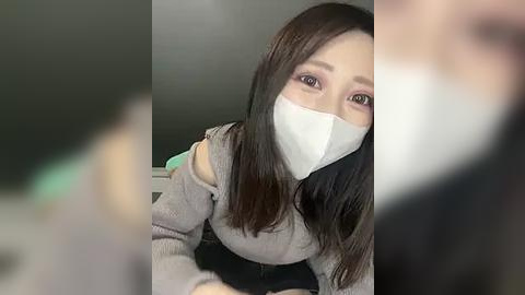 Media: Video of an Asian woman with long, straight black hair, wearing a gray off-shoulder sweater, a white face mask, and pink eyeshadow. She appears indoors, with a blurred background.