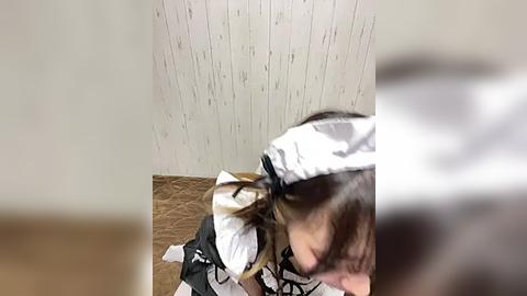 Media: A video of a person in a maid outfit, kneeling on a wooden floor with white wallpaper, wearing a white headband.