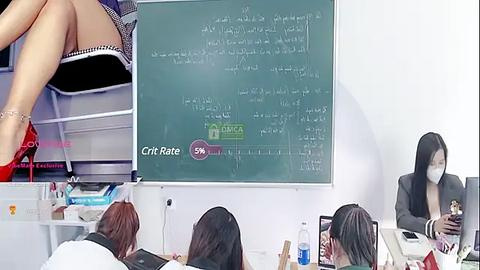 Media: Video of an Asian woman in a black suit and mask teaching math on a whiteboard, with students in red high heels and black blazers, desks cluttered with books.