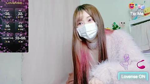 Media: Video of a young Asian woman with long, straight, brown hair, wearing a white face mask, pink fluffy robe, and a pink bedspread. Background includes a pink curtain and a white bed.