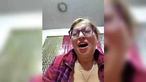 Media: A video of a woman with glasses, a pink jacket, and a necklace, laughing joyfully on a tiled floor with a blurred person in the background.