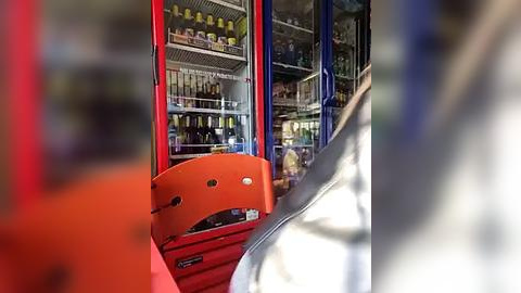 Media: Video of a bustling liquor store with an orange cash register in the foreground, shelves packed with bottles, and a person in the background.