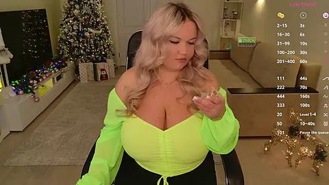 Media: Video of a curvy blonde woman with large breasts, wearing a neon green off-shoulder top, sitting in a living room with Christmas decorations.