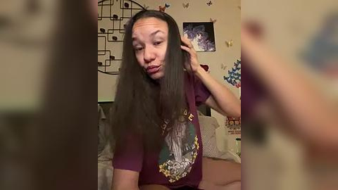 Media: Video of a young woman with long, dark hair, wearing a maroon T-shirt, adjusting her hair in a bedroom with a bed, butterfly stickers, and a TV on the wall.