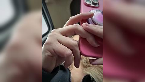 Media: A close-up video of a woman's hands holding a pink smartphone, with her fingers pressing buttons. Her face is partially visible, smiling, with blonde hair. The background is blurred, showing a car interior.