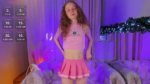 Media: A video of a young, slender Caucasian woman with long curly hair, wearing a pink crop top and mini skirt, standing in a purple-lit living room.