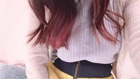 Media: A video showing a person with long, wavy, dark brown hair with red highlights, wearing a light gray ribbed sweater and yellow high-waisted pants with a black zipper.