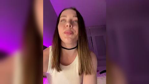 Media: Video of a young Caucasian woman with straight, shoulder-length brown hair, wearing a white tank top and black choker, indoors with purple lighting, blurred background.