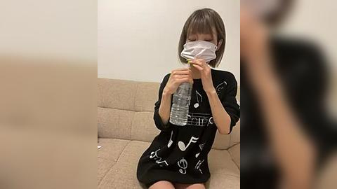 Media: Video of an East Asian woman with a short bob haircut, wearing a black dress with white print and a white face mask, drinking water from a plastic bottle on a beige couch.