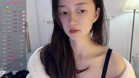 Media: Video of an East Asian woman with fair skin and long black hair, wearing a white off-shoulder sweater, standing indoors with blurred background, showcasing a chat interface on the left.