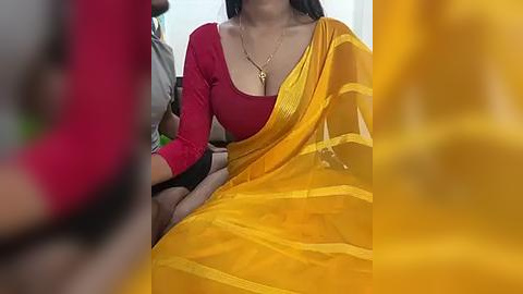 Media: Video of a woman in a vibrant orange sari with yellow stripes, wearing a red blouse, seated on a bus. Her long black hair is partially visible. Background is blurred.