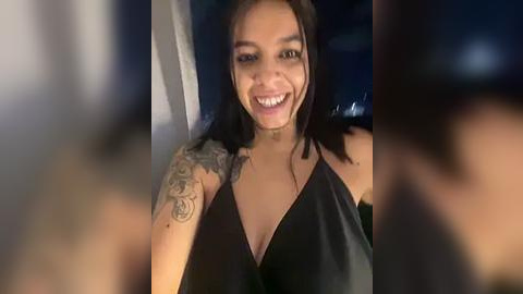 Media: A video of a smiling, light-skinned woman with long, dark hair and a black sleeveless top, showing off a detailed tattoo sleeve. The background is blurred, creating a focus on her joyful expression.