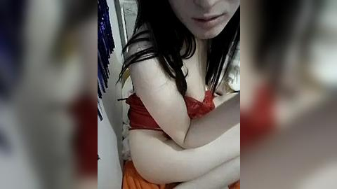 Media: A blurry, candid video of a young woman with pale skin and dark hair, wearing a red bra and orange pants, standing in a dimly lit room.